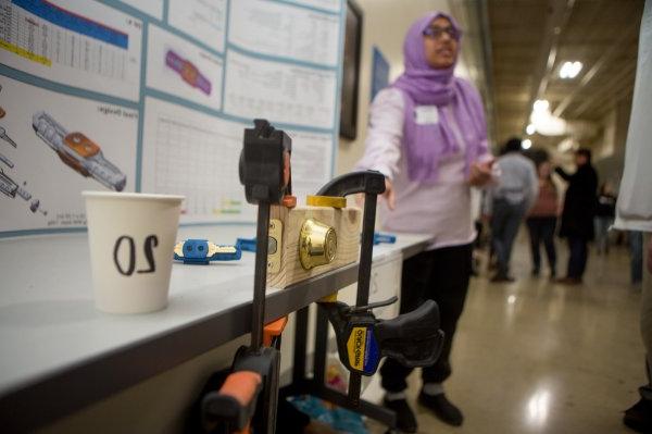 student in head scarf explains her project, a trifold poster is displayed on a table